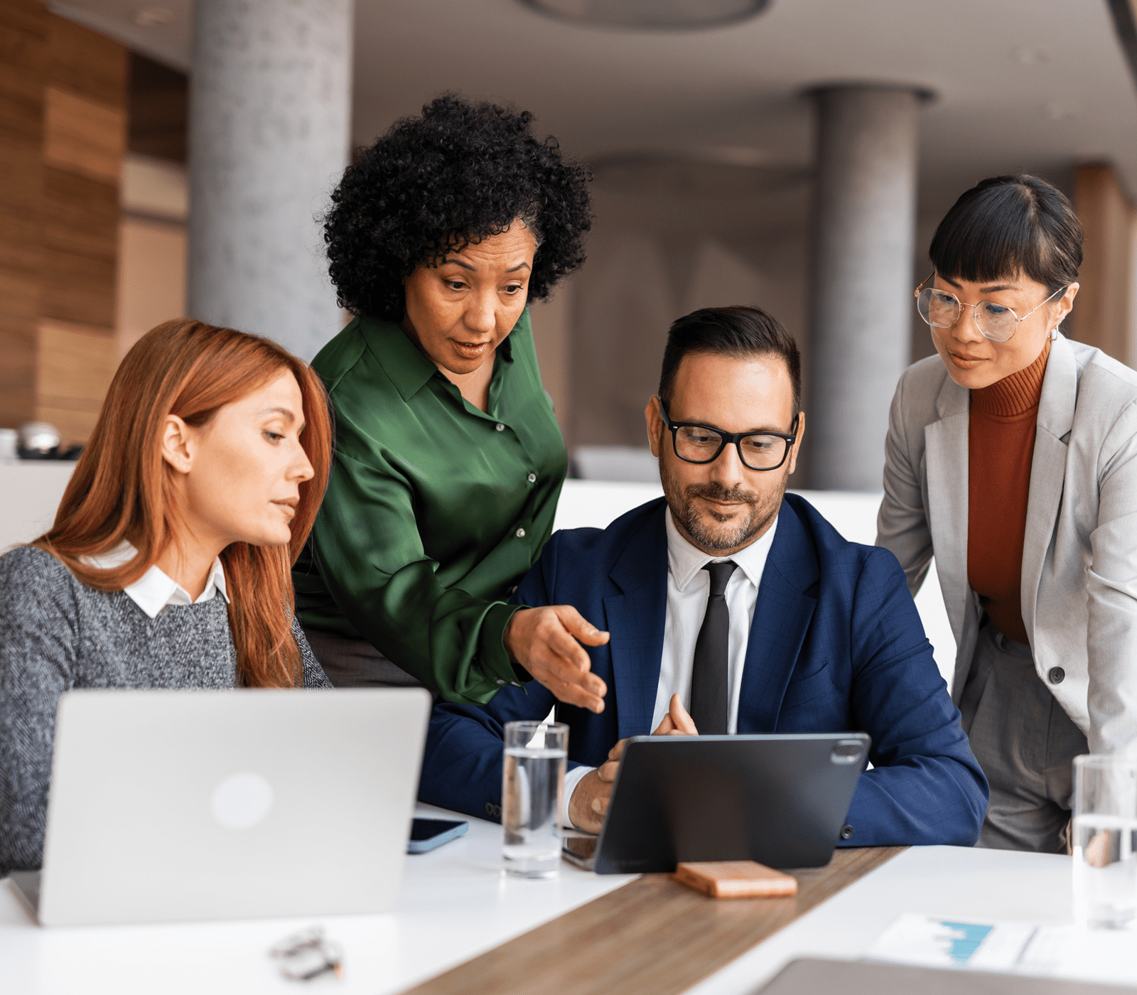 Four professionals collaborating over a tablet in a modern office.